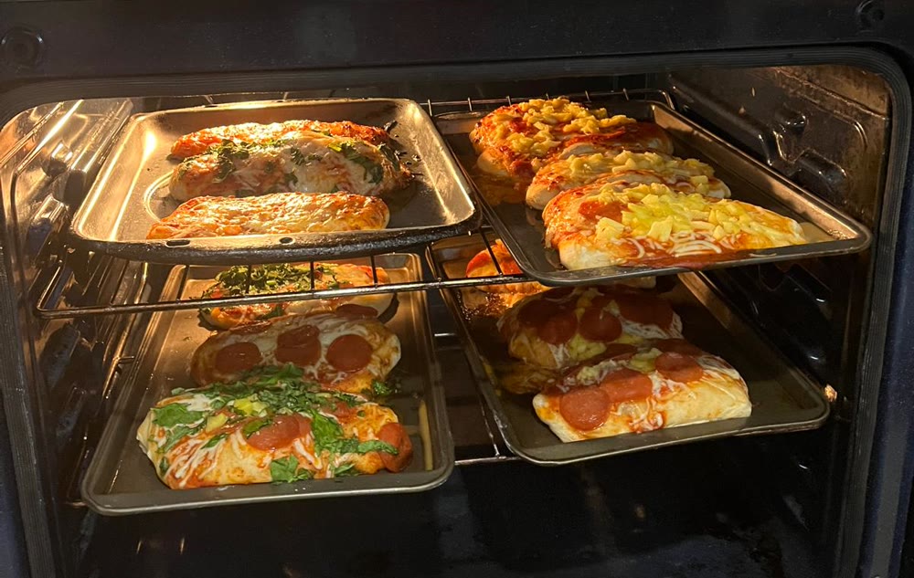 Homemade pizzas baking on four trays in the oven.